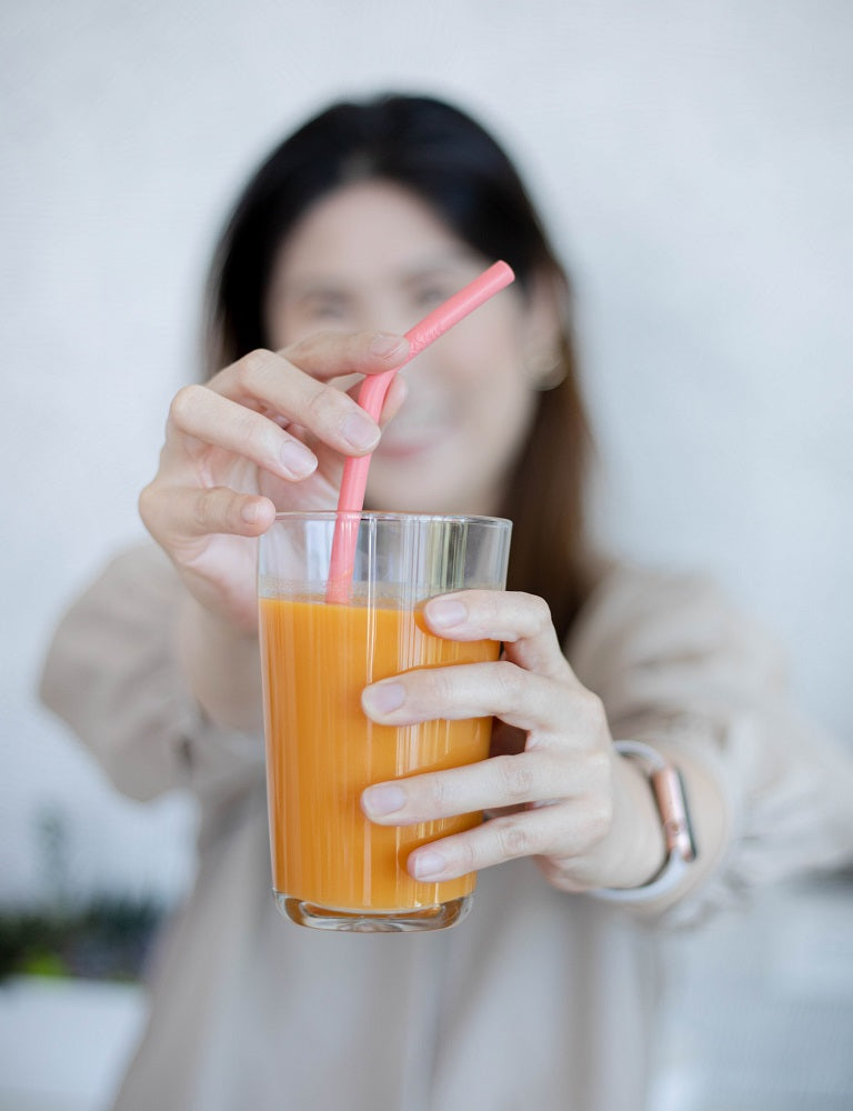 A woman holding a glass of orange juice with the Pink Living Coral Silicone Straw.