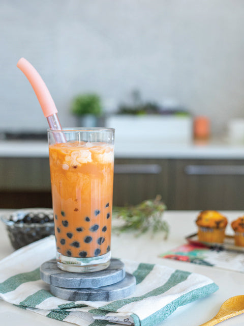 ReServe rose gold bubble tea straw in a glass of Thai iced tea with boba or pearl. The glass is placed on a table with some decorations around.