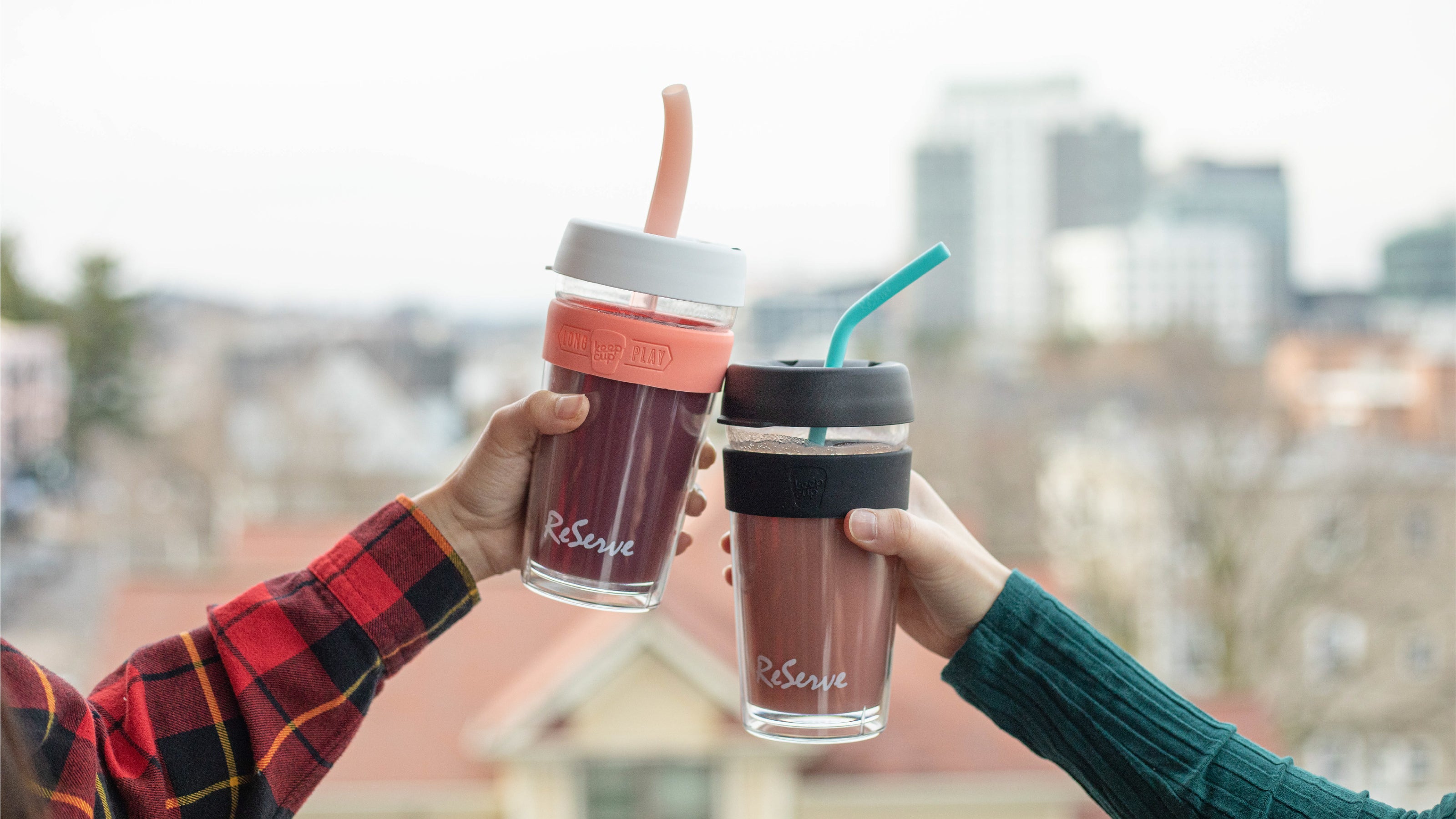 two hands holding ReServ KeepCup reusable cups with reusable silicone straw and bubble tea straw. The cups filled with fruity drinks.