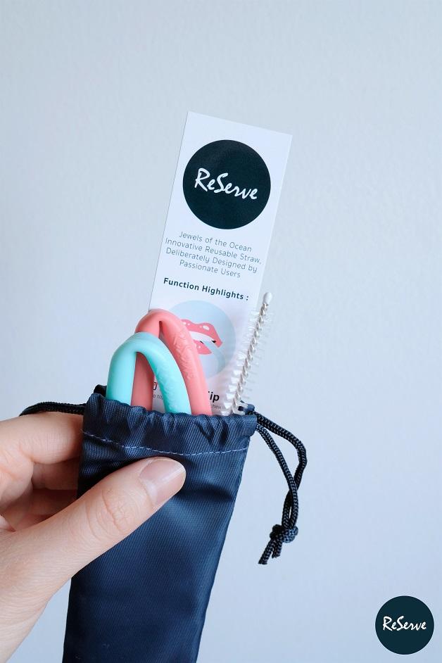 A hand holding ReServ pink and blue silicone reusable straws in a bag with label
